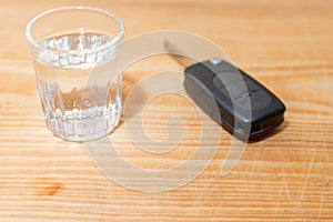 Glass of alcoholic drink and car key, on wooden table. key with glass of vodka on table.a glass of vodka and car keys.Indoors shot