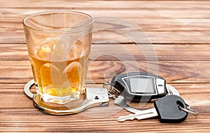 Glass with alcoholic drink, handcuffs and car key on wooden table