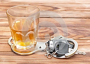 Glass with alcoholic drink, handcuffs and car key on wooden table