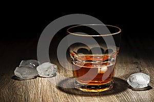 Glass of alcoholic drink with ice cubes on wooden table. Whiskey