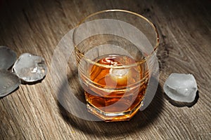 Glass of alcoholic drink with ice cubes on wooden table. Whiskey