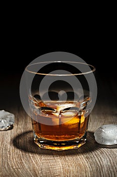 Glass of alcoholic drink with ice cubes on wooden table. Whiskey