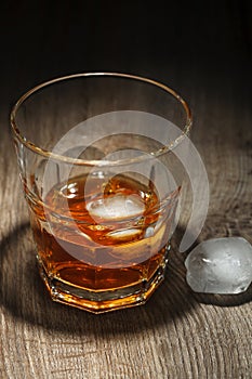 Glass of alcoholic drink with ice cubes on wooden table. Whiskey