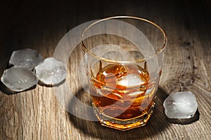 Glass of alcoholic drink with ice cubes on wooden table. Whiskey