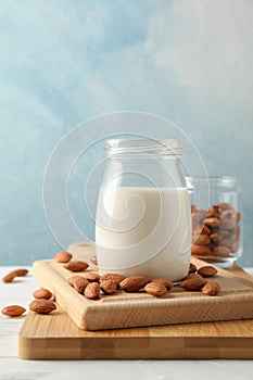Glass of almond milk, almond seeds on white table again blue background