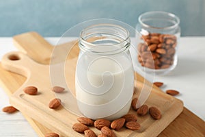 Glass of almond milk, almond seeds on white table again blue background