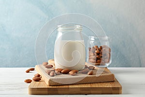 Glass of almond milk, almond seeds on white table again blue background