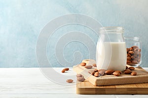 Glass of almond milk, almond seeds on white table again blue background