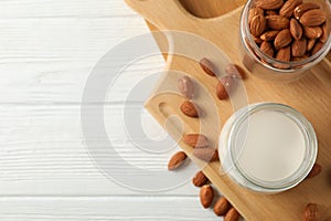 Glass of almond milk, almond seeds on white table again blue background, space for text