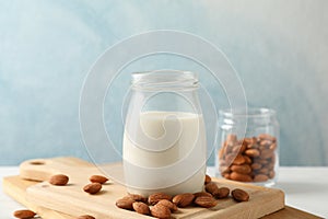 Glass of almond milk, almond seeds on white table again blue background, space for text