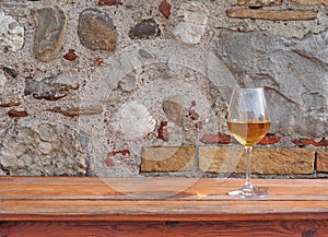 Glass of amber white wine on a rustic wooden table with an old stone wall behind. Background for copy space