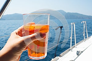 Glass of aperol spritz in the hand of a young woman, a boat trip