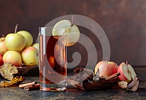 Glass of apple juice with juicy apples and cinnamon sticks on a kitchen table