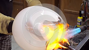 Glass artist fires a glass ball with a gas torch so that he can shape it by hand. Traditional method of shaping molten glass