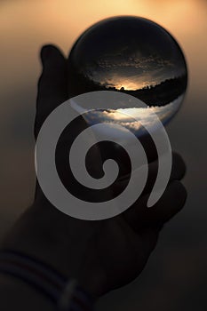 Glass ball in hand with sunset reflection