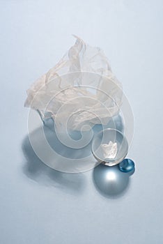 Glass ball, piece of white organza textile and blue pebble on blue background