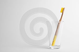 Glass with bamboo toothbrush on white background.