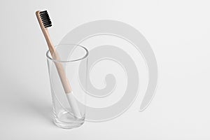 Glass with bamboo toothbrush on white background.