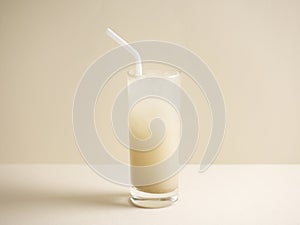 A glass of barley water with straw isolated on grey background side view