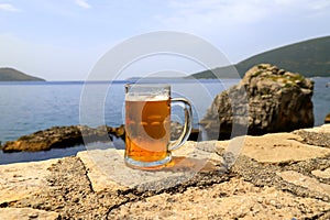 Glass of beer on background of sea, close-up. A fogged mug, a glass of cold beer stands against of sea and mountain landscape in
