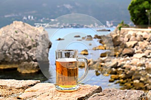 Glass of beer on background of sea, close-up. A fogged mug, a glass of cold beer stands against of sea and mountain landscape in
