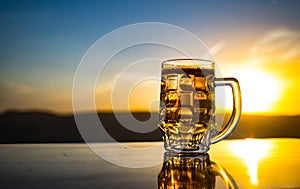 Glass of beer on a beach at sunset. Cooling summer drink concept. Close Up of A Glass of Draught Beer with the Bokeh of Sunlight