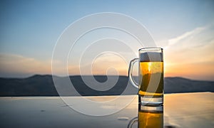 Glass of beer on a beach at sunset. Cooling summer drink concept. Close Up of A Glass of Draught Beer with the Bokeh of Sunlight