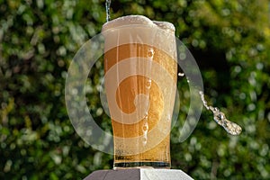 Glass of beer being overfilled with foam and bubbles flowing dow