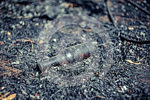 A glass beer bottle lies on the scorched ground