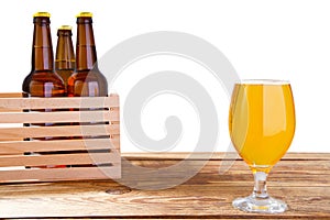 Glass of beer and bottles with no logo on wooden table isolated copy space, glass bottle