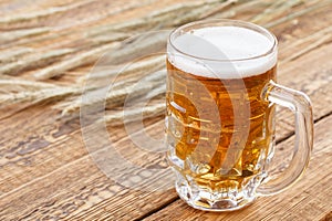 Glass of beer with ears of barley on a wooden background