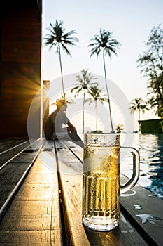 A glass of beer filled with cold drinks and ice placed on a wooden deck