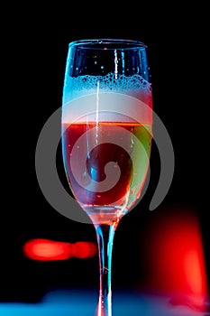 glass of beer with foam on with red light. water drops on the glass.