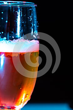 glass of beer with foam on with red light. water drops on the glass.