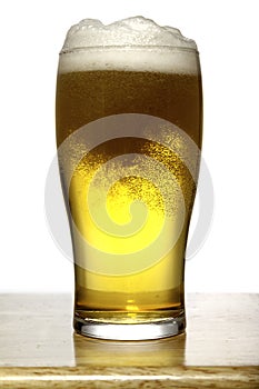 Glass of beer with foam on wood and white background