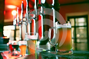 Glass, beer mug filled with golden-colored lager or pilsner foamy beer. Blurred background of bar, pub atmosphere