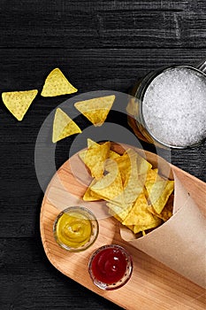 Glass of beer with nachos chips on a wooden background.