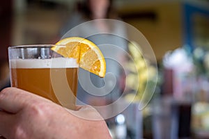 Glass of beer with orange slice garnish in a man`s hand
