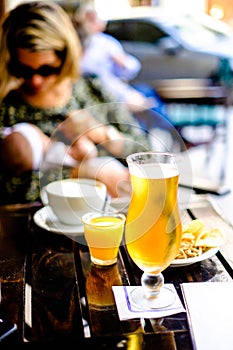 Glass of beer in outside pub, woman and baby in the background,