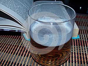 A glass of beer and pages of an open book. A pleasant rest while reading. The book is very interesting to read it is a pleasur