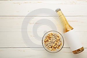 Glass of beer with peanuts on white wooden background