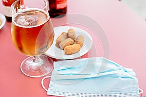 Glass of beer and a plate of tapas with a mask on the table