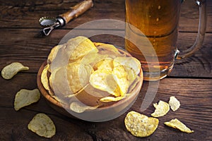 Glass of beer, potato chips in a bowl on a dark wooden background. Pouring light beer in a glass.