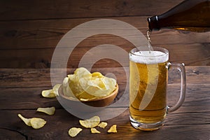 Glass of beer, potato chips in a bowl on a dark wooden background. Pouring light beer in a glass.