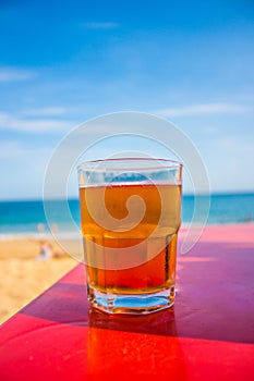 Glass of beer on red table at the shore of the beach photo