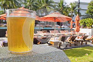 Glass of beer on resort swimming pool background.