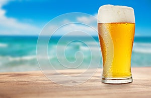 Glass of beer on wooden table on background of sea