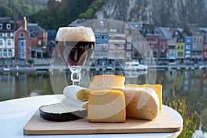 Glass of Belgian abbey beer and tasting of cheeses made with trappist beer and fine herbs with view on Maas river in Dinant,