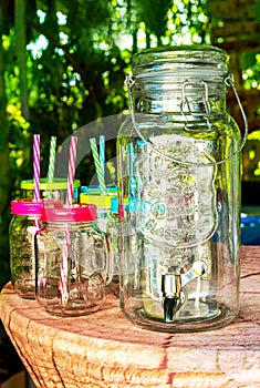 Glass Beverage Drink Dispenser, Glasses with Handle, colored Lids and Straws decorated on a table