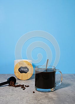 A glass of black coffee and a bowl with stevia sweetener, blue background